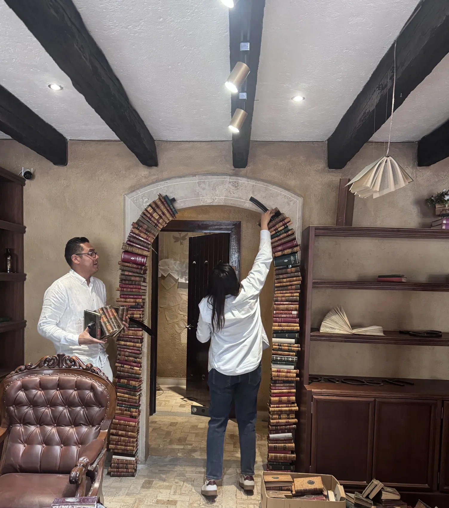 Arco construido con lomos de libros antiguos alrededor de una puerta, junto a un sillón capitoneado de piel.