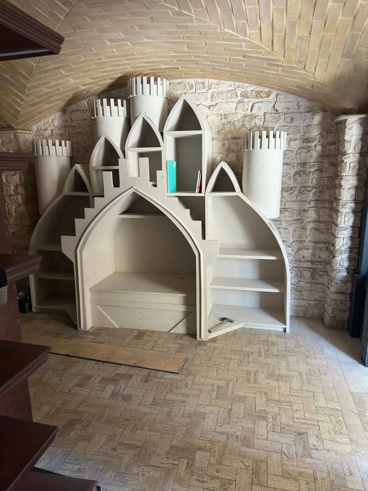 Librero en forma de castillo blanco con torres y arcos, bajo una bóveda de ladrillo.
