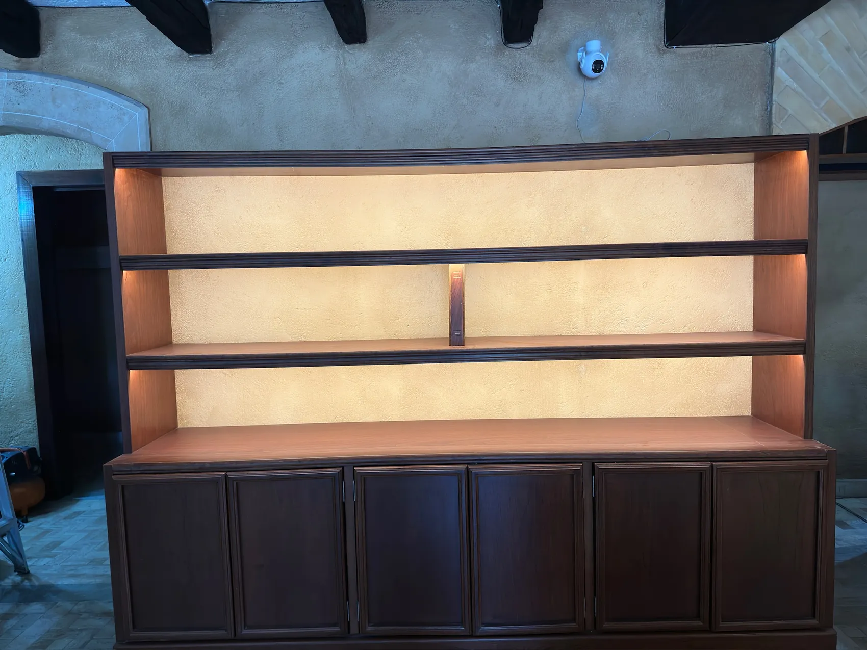 Estantería de madera oscura iluminada por dentro, esperando los libros.